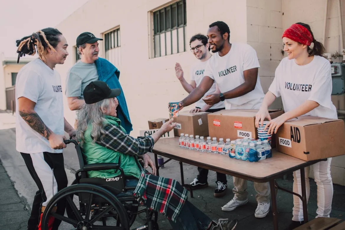 A Group of Volunteering people helping an Elderly Person on a Black Wheelchair For Charity